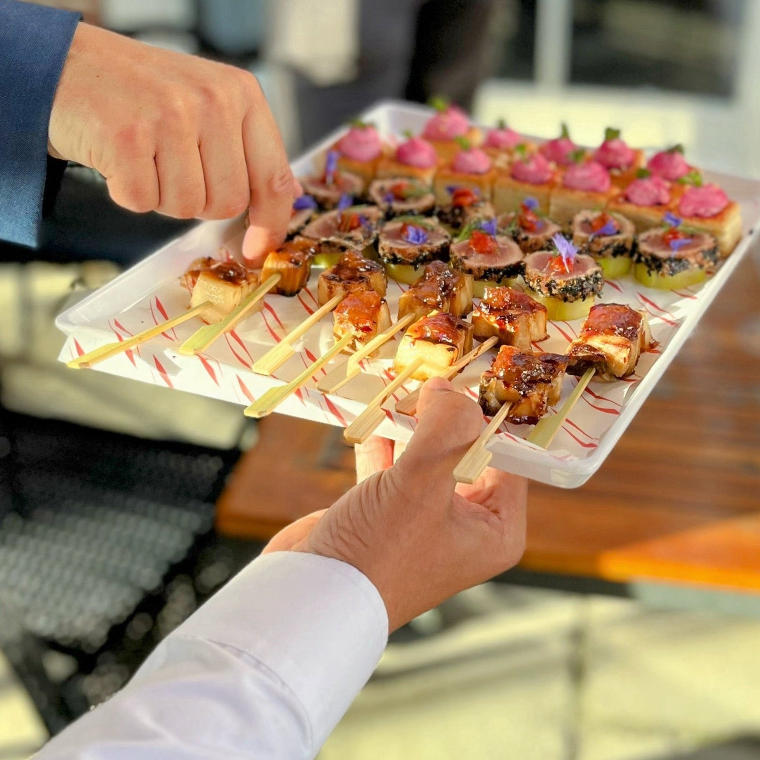 Tray of skewered appetizers being held by a person outdoors